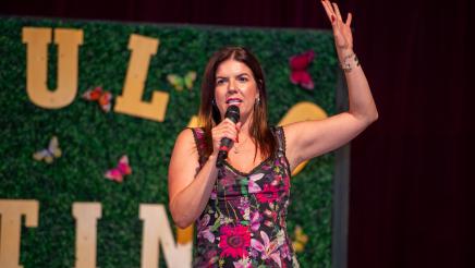 Fernanda Kelly holding microphone, speaking and raising one arm upward