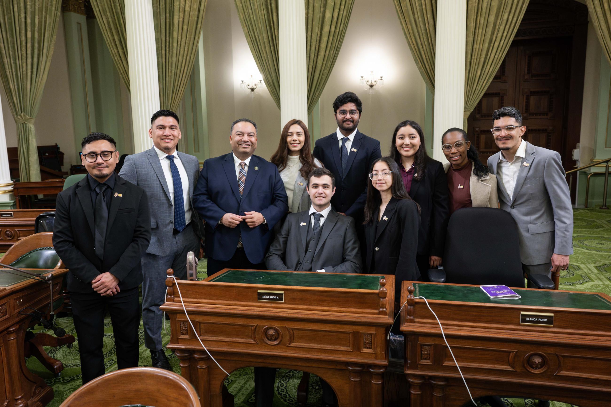 Group photo of Asm. Solache with student group, standing around desk