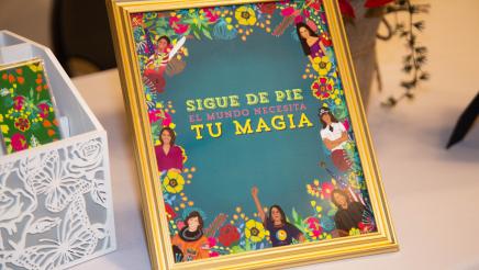 Framed "Sigue de Pie El Mundo Necesita Tu Magia" display on table