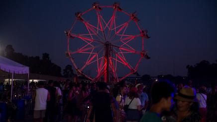 Attendees with large ferris wheel with red lights in background