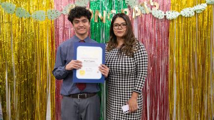 Student holding up certificate, with parent, in front of festive background