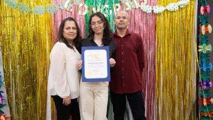 Student holding up certificate, with parents, in front of festive background