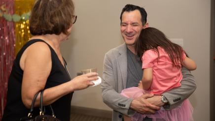 Speaker Emeritus Rendon holding daughter and sharing a light moment with attendee