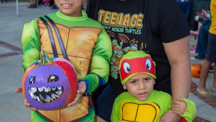 Mother with two kids wearing costumes, one holding painted pumpkin