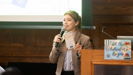 Emcee holding microphone, speaking, with large screen in background