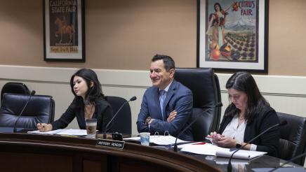 Speaker Emeritus Rendon seated at desk, sharing a light moment with witness