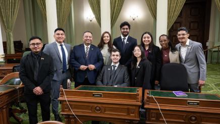 Group photo of Asm. Solache with student group, standing around desk