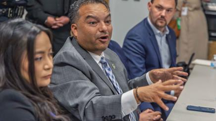 Asm. Solache seated at table, speaking and gesturing with both hands