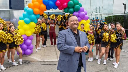 Asm. Solache in front of rainbow ballon arch, with drill team at sides