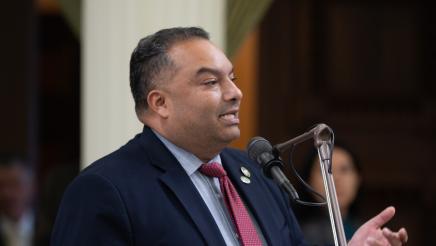 Asm. Solache standing at microphone, speaking and gesturing with one hand