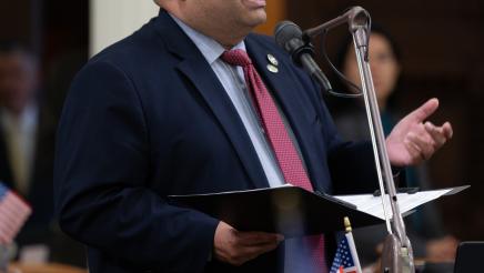 Asm. Solache standing at microphone, speaking and gesturing with one hand